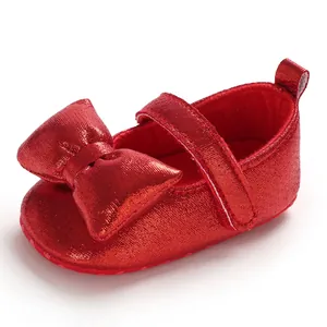 Detailed shot of shiny red infant princess shoes with a large bow and soft sole