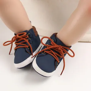 Gros plan de chaussures montantes pour bébé bleu marine avec semelles souples et lacets orange