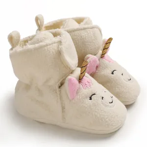 Primo piano di stivaletti in peluche per neonati con ricamo unicorno e corno dorato.