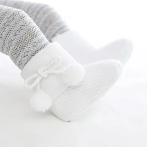 Gros plan sur des bottines bébé en tricot blanc avec semelles souples et pompons décoratifs