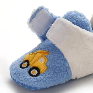 Detail of blue fleece baby shoe featuring a yellow truck embroidery and velcro straps.