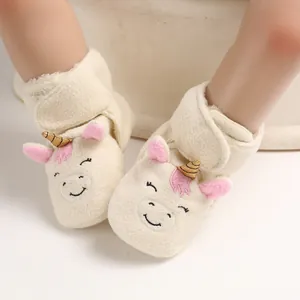 Primo piano di scarpine neonato in peluche con design unicorno e morbido pile crema.