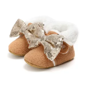 Detail von braunen Plüsch-Babystiefeln mit goldener Paillettenschleife und weißem Fell