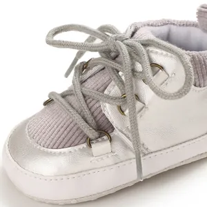 Détail d'une chaussure bébé argentée montrant le velours côtelé et les lacets doux.