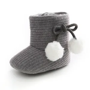 Vue détaillée de bottes tricotées pour bébé grises avec pompons blancs et nœud