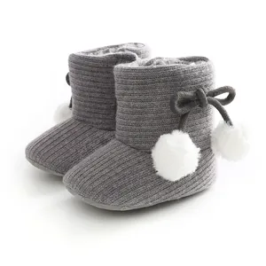 Bottes de bébé en tricot gris avec pompons blancs et doublure en polaire chaude.