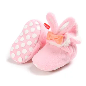 Detail van roze pluche babyschoenen met konijnenoren en antislipzooltjes.