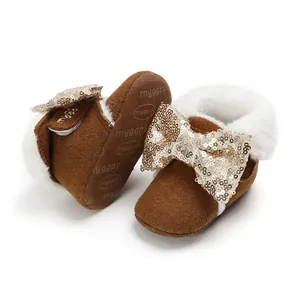 Nahaufnahme von Babystiefeln mit goldener Paillettenschleife und weißem Kunstpelzfutter.