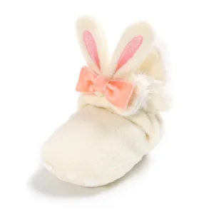Close-up van een crème pluizige babyschoen met konijnenoren en een roze fluwelen strik
