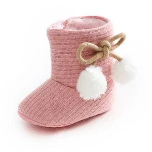 Détail d'un chausson pour bébé en tricot rose avec des pompons blancs et une doublure chaude