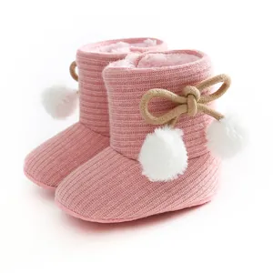 Détail de bottes pour bébé en tricot rose avec pompons blancs et doublure douce.