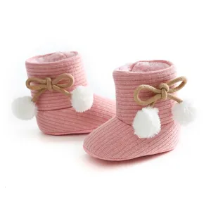 Détail de bottes d'hiver roses tricotées pour bébé avec pompons et semelles souples.
