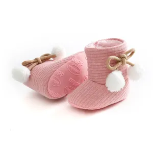 Vue détaillée de bottines en tricot rose pour bébé avec pompons blancs et semelles souples.