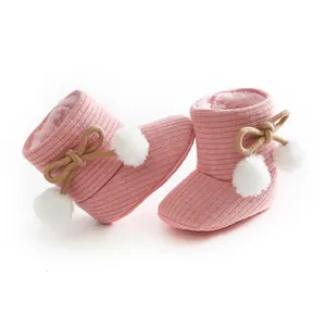Vue détaillée de bottes d'hiver pour bébé en tricot rose avec pompons blancs et un nœud doux