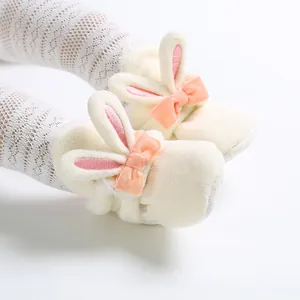 Close-up van zachte pluche babyslofjes met schattige roze konijnenoren en strikjes.