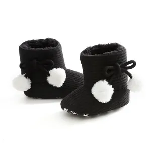 Gros plan de bottes d'hiver noires pour bébé avec des semelles souples et des pompons.