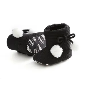 Gros plan sur des bottes d'hiver en tricot noir pour bébé avec pompons et nœud blanc