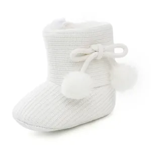 Détail de bottine en tricot blanche pour bébé avec pompons doux et doublure peluche