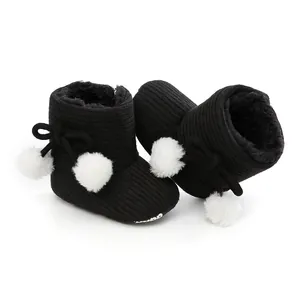 Détail de la texture en maille et du pompon blanc sur les bottines d'hiver noires pour bébé