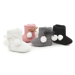 Détail des bottes d'hiver pour bébé avec pompons et semelles souples en plusieurs couleurs.