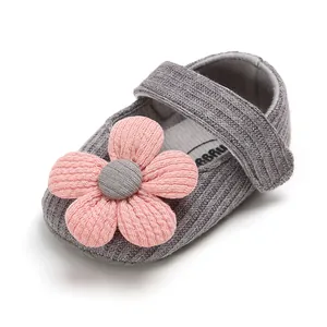 Close-up of a grey knitted baby girl shoe with a large pink fabric flower detail