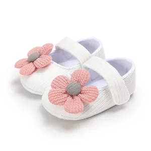 Detail view of soft-sole white knitted baby girl shoes with pink flower decoration.