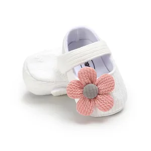 Detail view of soft white yarn baby shoes featuring a large pink decorative flower.