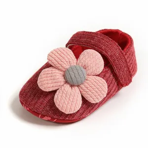 Close-up of red knitted baby girl princess shoe with a large pink flower decoration