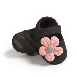 Close-up detail of soft black ribbed baby girl shoes with a large pink knitted flower