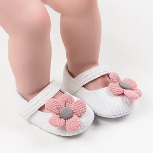 Close-up of white knit baby girl shoes with large pink flower ornament