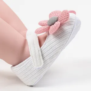 Close-up of white knitted baby girl princess shoe featuring a cute pink flower detail