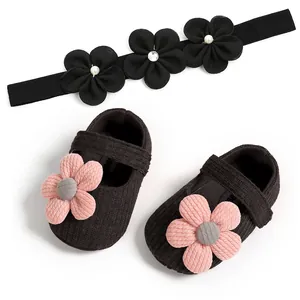 Close-up of black corduroy baby girl shoes with pink knitted flowers and headband