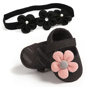 Close-up detail of black knitted baby girl princess shoes with pink flower and headband
