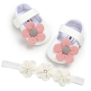 Detailed view of white knitted baby princess shoes with pink flowers and a matching headband.
