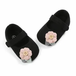 Detail view of black baby girl princess shoes featuring a pink knit flower with button.