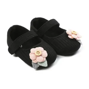 Close-up detail of soft knitted black baby girl shoes with pink floral button design