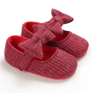 Detailed close-up of soft knitted red baby princess shoes with a large delicate bow decoration.