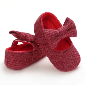 Close-up of red knitted baby walker shoes with decorative bow detail and soft sole.