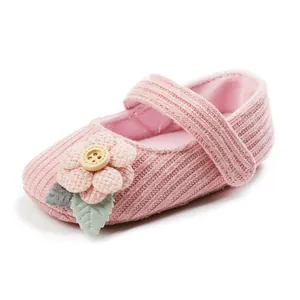 Close-up of pink knitted baby princess shoe with fabric flower and wooden button detail.
