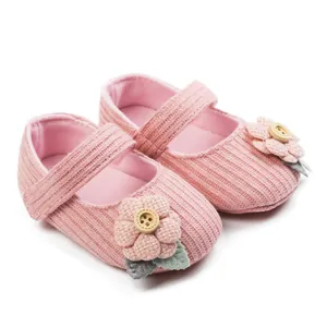 Close-up detail of pink knitted baby shoes featuring cute flower appliques and wooden buttons.