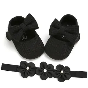 Detalle de zapatos de bebé de punto negro con lazo grande y diadema de flores a juego