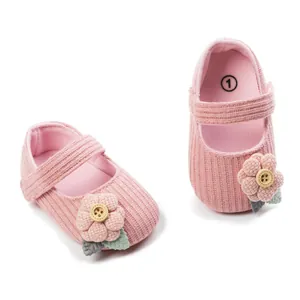 Detail of pink knit baby princess shoes with fabric flower and button decoration.