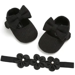 Detalle de zapatos de bebé de punto negro con lazo y conjunto de diadema floral a juego