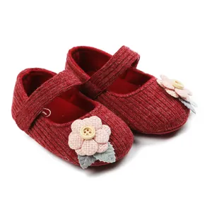 Close-up of red knitted baby shoes with pink fabric flower and wooden button detail
