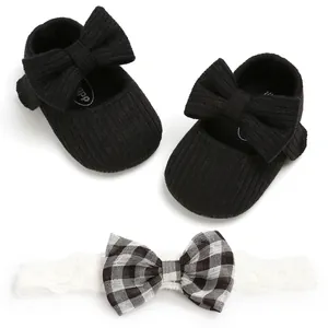 Close-up view of black knitted baby girl shoes and matching plaid bow headband set