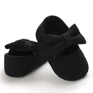 Close-up of black ribbed infant princess shoes featuring a large decorative bow detail.