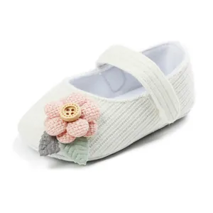 Detailed view of a white knit infant shoe with a pink fabric flower and wooden button.