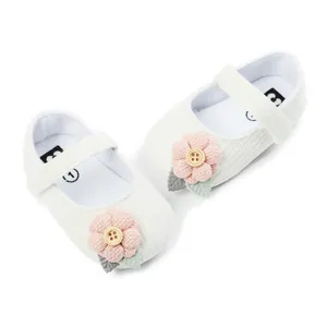 Macro view of pink fabric flower and wooden button on white knitted baby Mary Janes