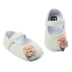 Close-up of white knit baby princess shoes featuring pink fabric flowers and buttons