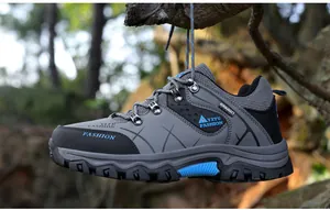 Side profile of a grey and black outdoor hiking shoe hanging from a tree branch in a forest